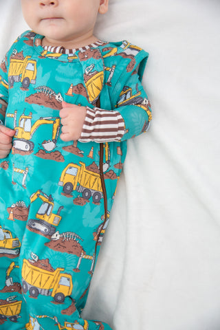Baby wearing a onesie with construction vehicle pattern on a white background