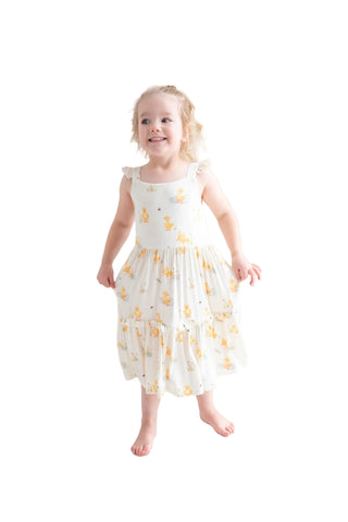 Young girl in a white dress with yellow floral pattern standing on a white floor.