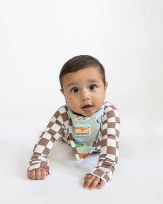 Baby wearing a brown and white checkered outfit with a colorful bib on a white background