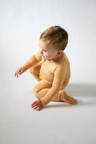 Child wearing a yellow onesie sitting on a white background