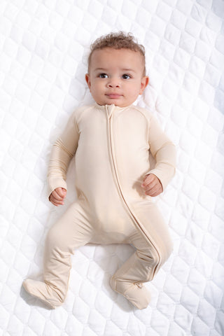 Baby wearing a beige onesie on a white textured surface