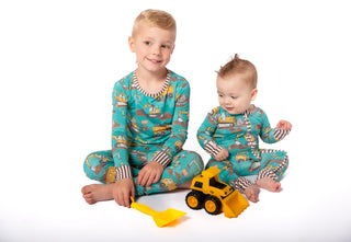 Two children wearing matching pajamas with vehicle patterns, sitting on a white background.